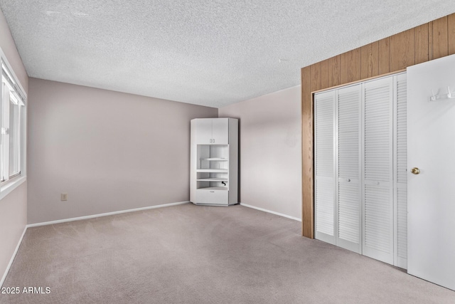 unfurnished bedroom with light carpet, a closet, a textured ceiling, and wood walls