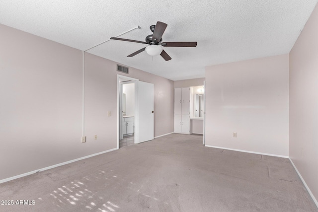 unfurnished bedroom featuring ceiling fan, light colored carpet, ensuite bath, and a textured ceiling