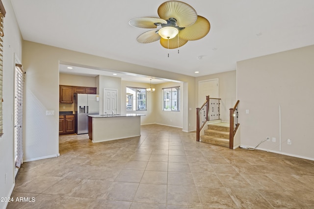 interior space with light tile patterned flooring, ceiling fan with notable chandelier, a kitchen island, sink, and stainless steel fridge with ice dispenser