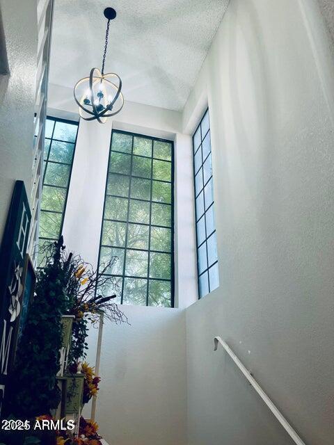 staircase with a textured ceiling, a healthy amount of sunlight, and a chandelier