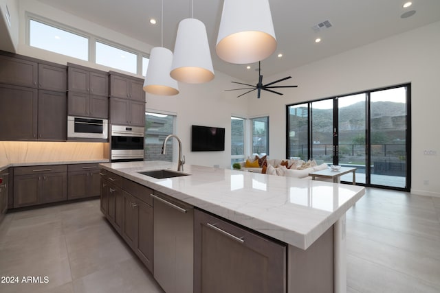 kitchen with stainless steel appliances, a center island with sink, sink, a towering ceiling, and pendant lighting