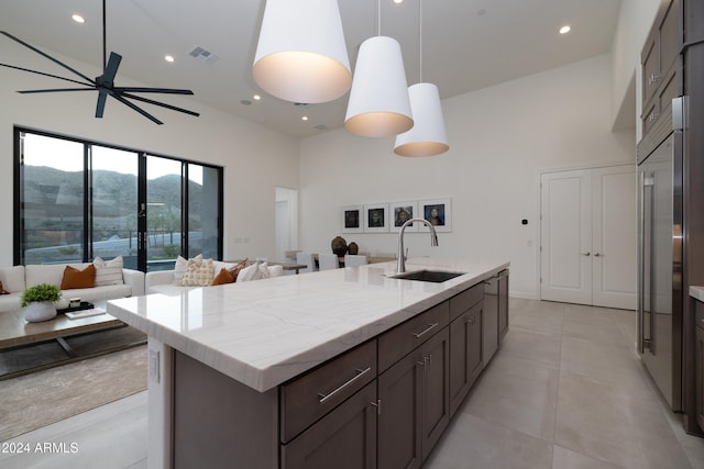 kitchen featuring hanging light fixtures, a towering ceiling, sink, and an island with sink