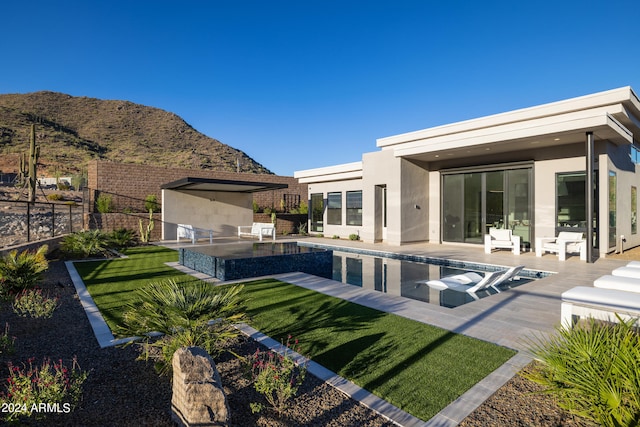 back of property with a mountain view, an outdoor kitchen, a lawn, and a patio area