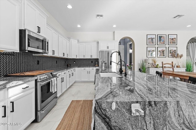 kitchen featuring stainless steel appliances, white cabinets, dark stone counters, and sink