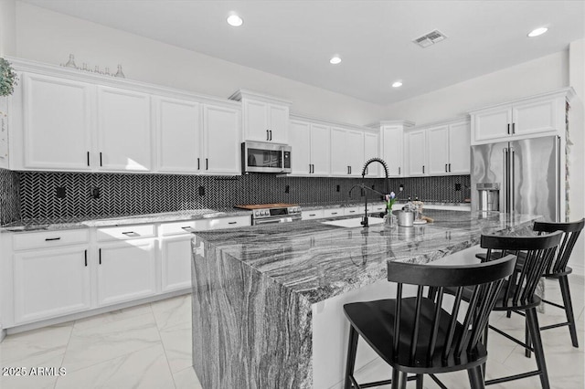 kitchen with a center island with sink, appliances with stainless steel finishes, stone countertops, white cabinets, and a breakfast bar