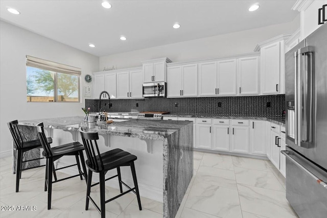 kitchen with white cabinetry, a center island with sink, a breakfast bar area, appliances with stainless steel finishes, and dark stone countertops