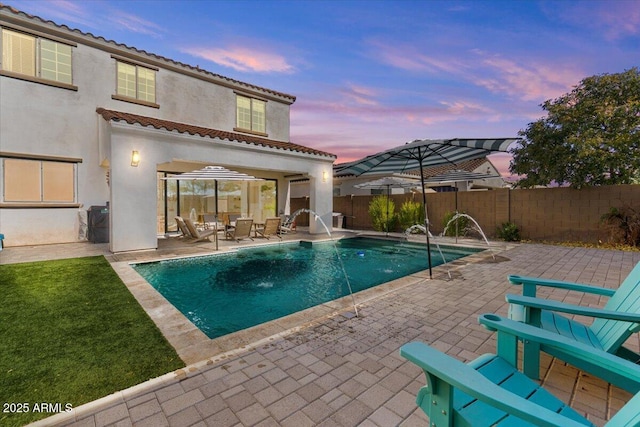 pool at dusk with pool water feature and a patio