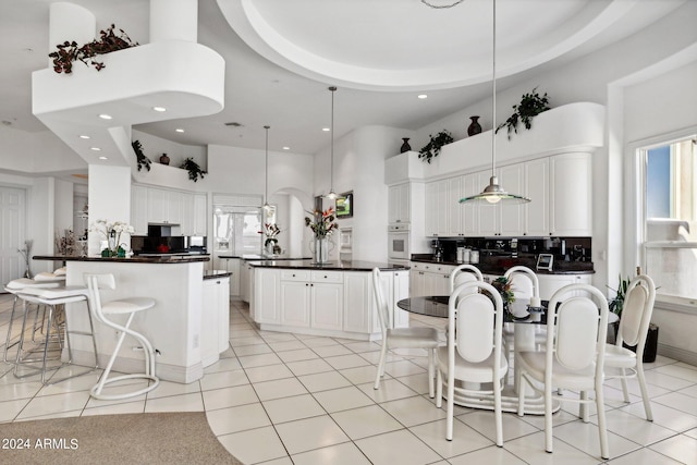 kitchen with pendant lighting, white cabinets, a high ceiling, a center island, and light tile patterned flooring