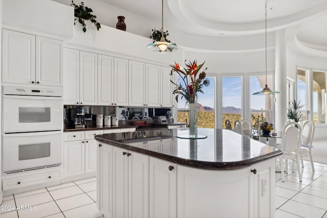 kitchen with white cabinets, pendant lighting, a center island with sink, and double oven