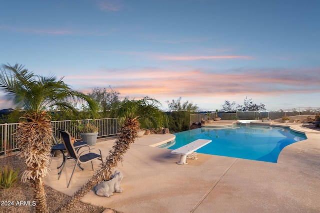 pool at dusk with a patio area and a diving board