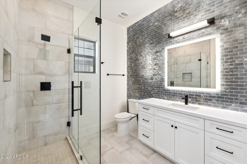 bathroom with toilet, vanity, a shower with shower door, and backsplash