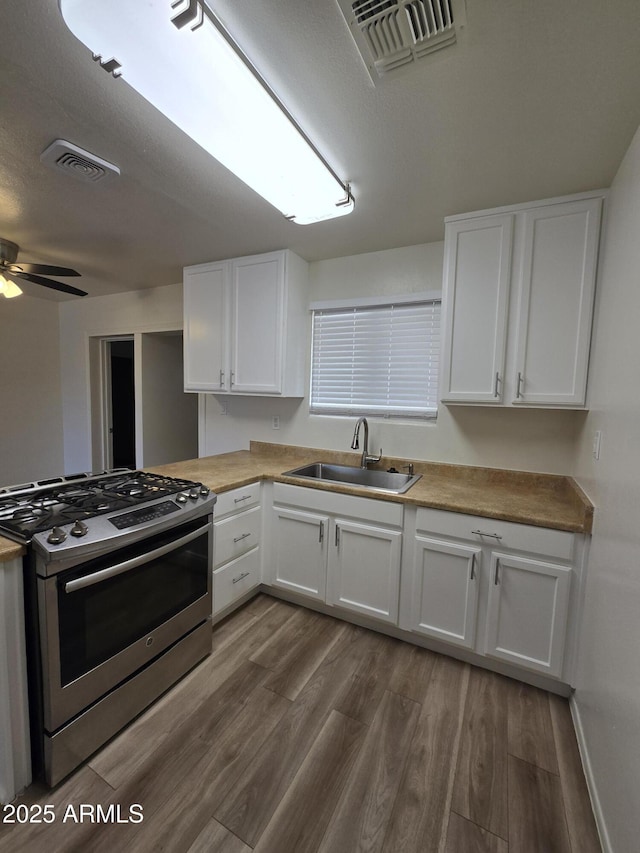 kitchen featuring white cabinets, stainless steel range with gas cooktop, sink, ceiling fan, and wood-type flooring