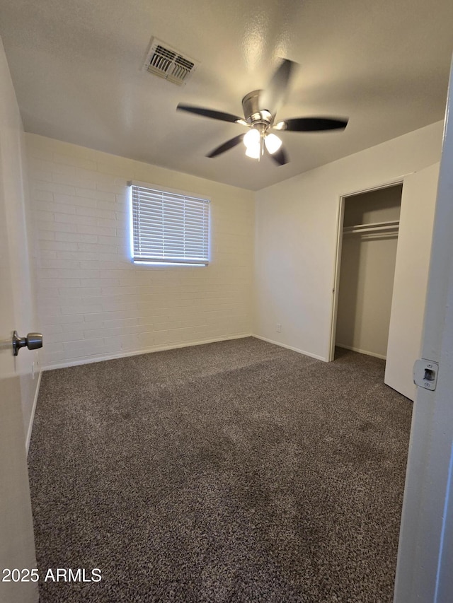 unfurnished bedroom featuring dark colored carpet, ceiling fan, brick wall, and a closet