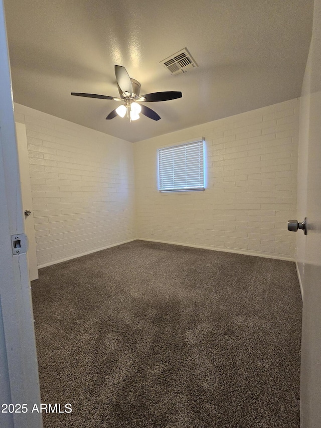 carpeted empty room featuring ceiling fan and brick wall