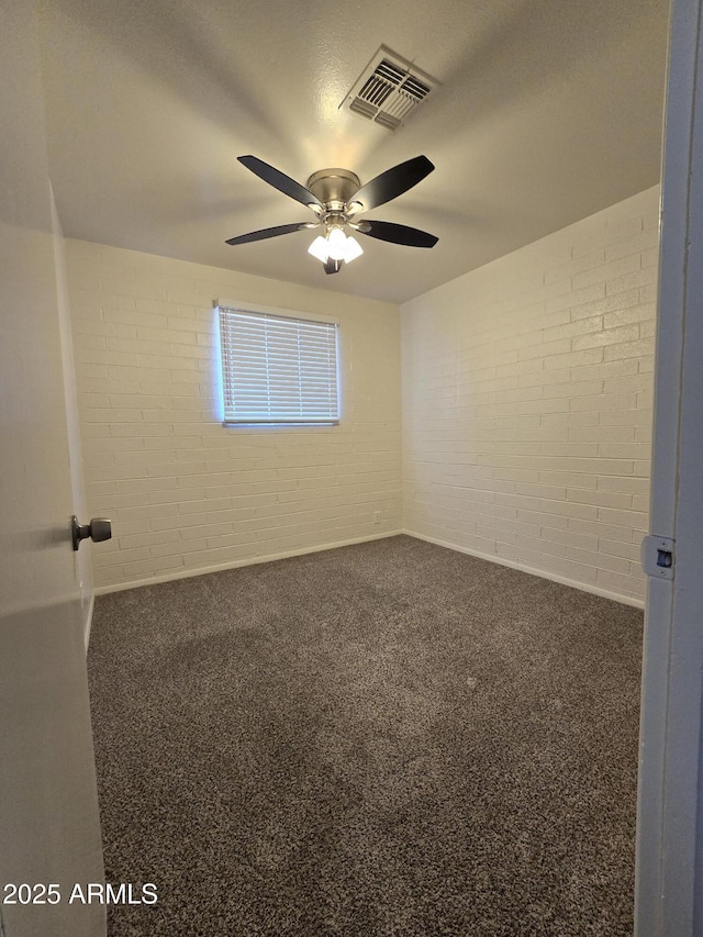 carpeted empty room with ceiling fan and brick wall