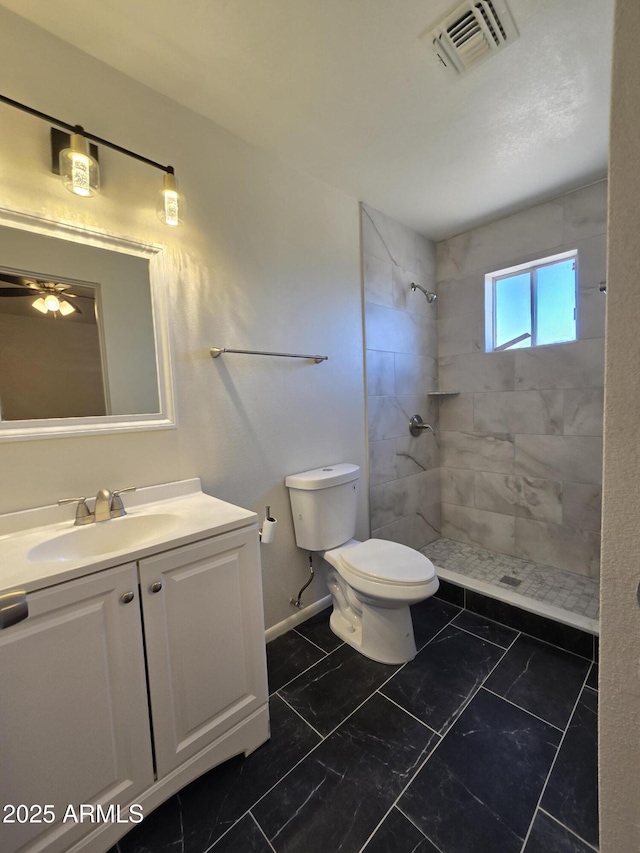 bathroom with vanity, toilet, and tiled shower