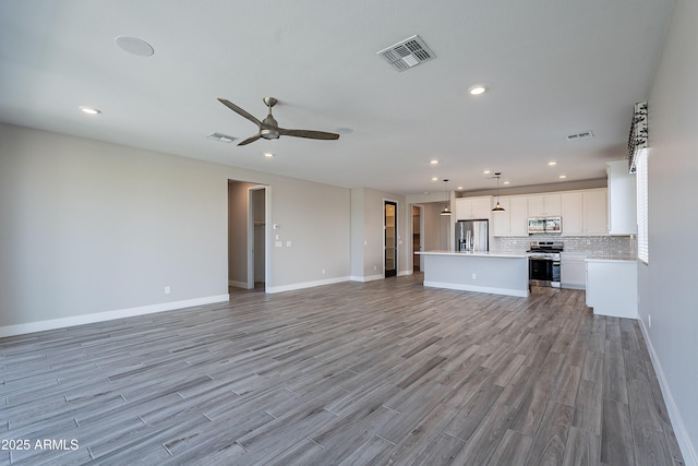 unfurnished living room with a ceiling fan, recessed lighting, light wood-style floors, and baseboards