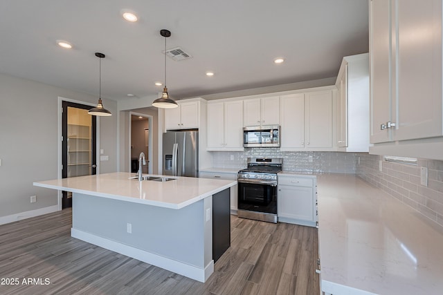 kitchen featuring appliances with stainless steel finishes, a sink, light wood-style flooring, tasteful backsplash, and white cabinetry