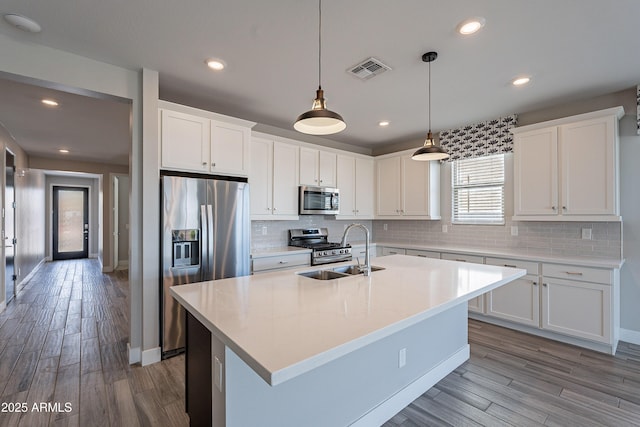 kitchen featuring appliances with stainless steel finishes, a sink, tasteful backsplash, wood finished floors, and white cabinets