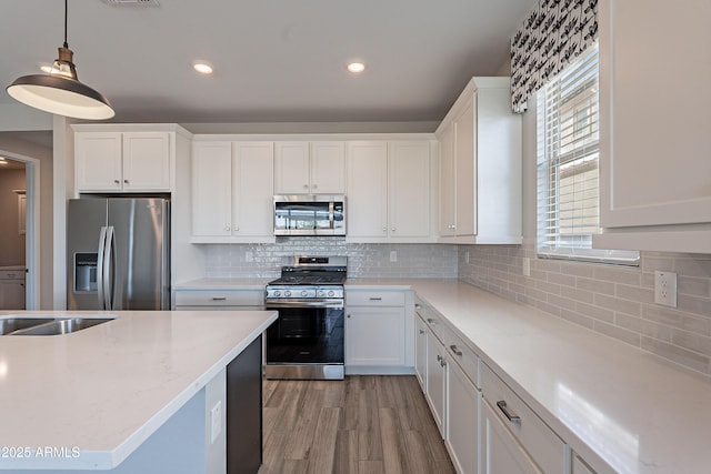 kitchen featuring appliances with stainless steel finishes, white cabinets, hanging light fixtures, tasteful backsplash, and recessed lighting