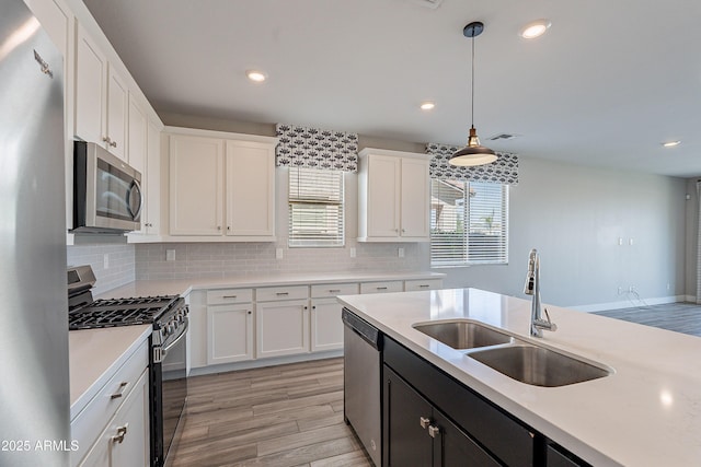 kitchen with stainless steel appliances, light countertops, light wood-type flooring, white cabinetry, and a sink