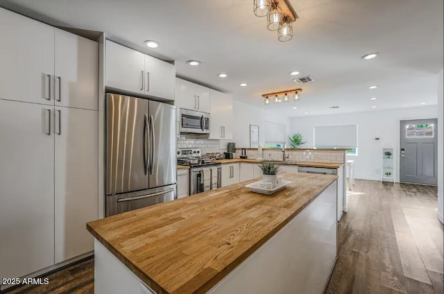 kitchen featuring dark wood-style floors, wooden counters, decorative backsplash, appliances with stainless steel finishes, and a peninsula