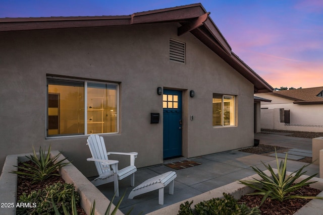 back of house at dusk with a patio area and stucco siding