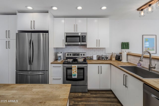 kitchen with stainless steel appliances, a sink, wooden counters, and white cabinetry