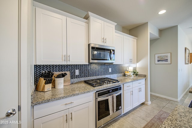 kitchen with baseboards, white cabinetry, light stone countertops, decorative backsplash, and stainless steel appliances