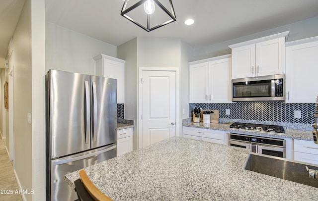 kitchen with white cabinets, baseboards, appliances with stainless steel finishes, backsplash, and light stone counters