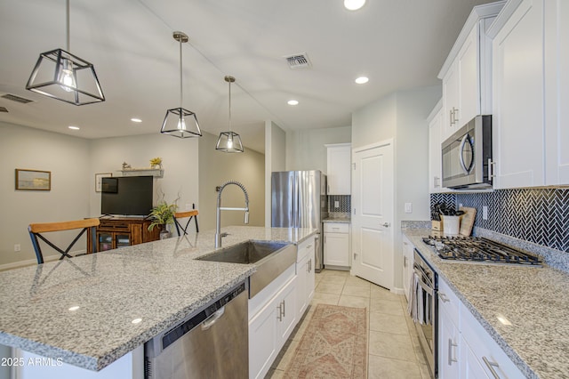 kitchen with visible vents, a sink, appliances with stainless steel finishes, a kitchen island with sink, and backsplash