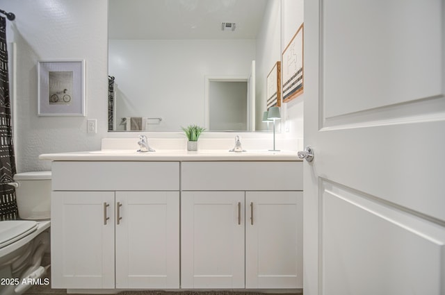 bathroom featuring toilet, double vanity, a sink, and visible vents