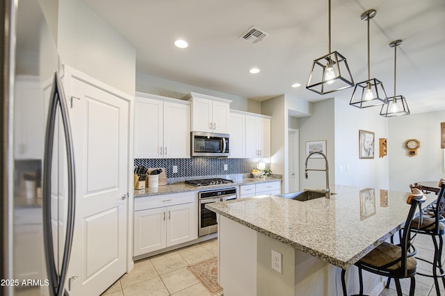 kitchen featuring an island with sink, backsplash, visible vents, stainless steel appliances, and a sink