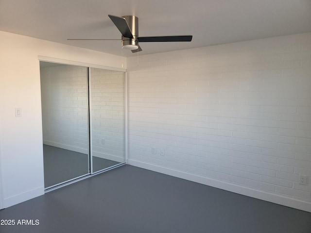 unfurnished bedroom with finished concrete flooring, ceiling fan, a closet, and baseboards