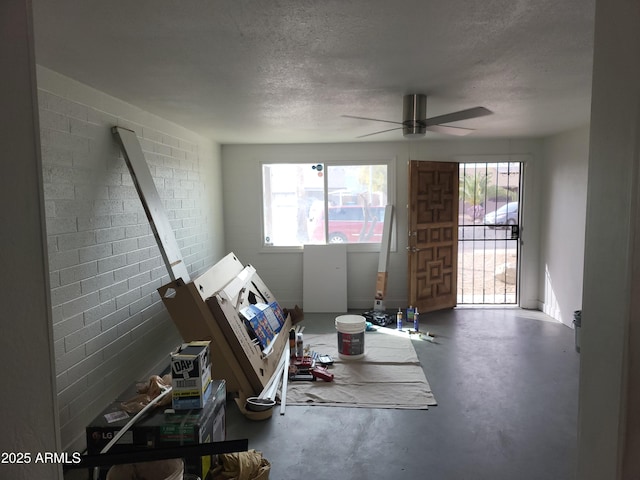 interior space with plenty of natural light, a textured ceiling, a ceiling fan, and concrete flooring