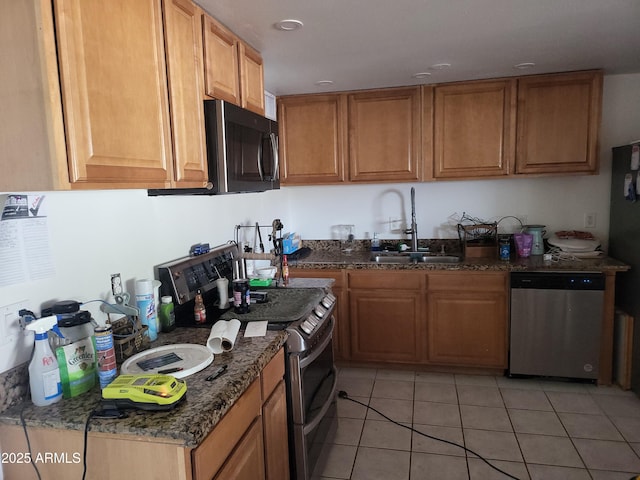 kitchen with dark stone countertops, stainless steel appliances, sink, and light tile patterned floors