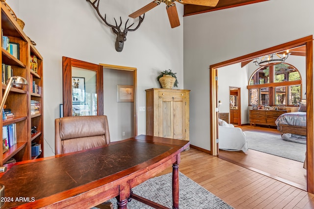 home office with hardwood / wood-style floors, a towering ceiling, and ceiling fan