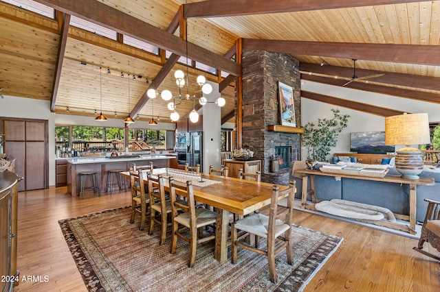 dining space with a stone fireplace, beam ceiling, high vaulted ceiling, light hardwood / wood-style floors, and wooden ceiling