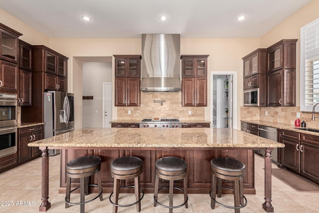 kitchen featuring sink, a center island, dark brown cabinetry, stainless steel appliances, and wall chimney range hood