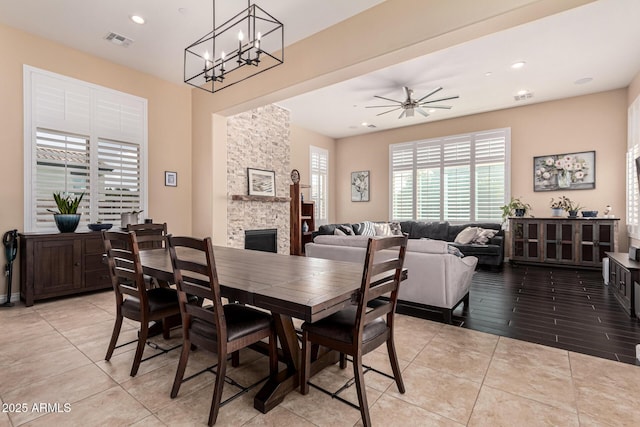 tiled dining area featuring a stone fireplace and ceiling fan with notable chandelier