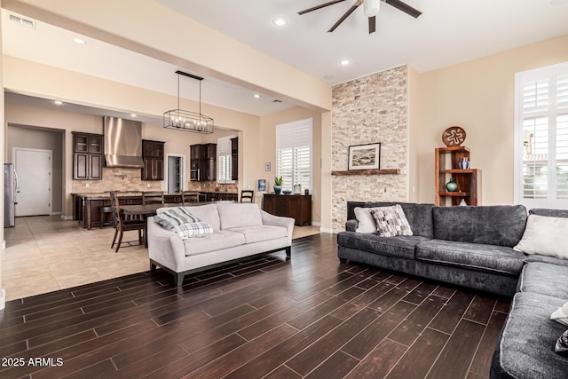 living room featuring dark wood-type flooring, ceiling fan, and a stone fireplace