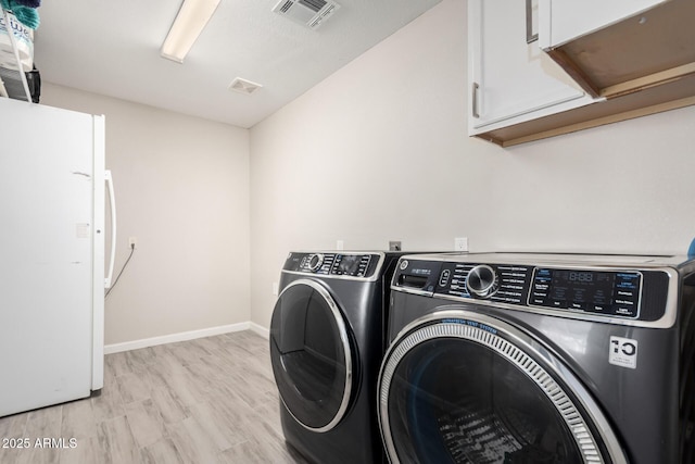 laundry room featuring visible vents, independent washer and dryer, baseboards, light wood-type flooring, and cabinet space