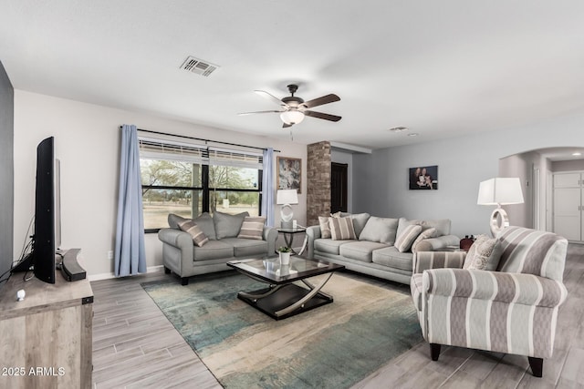 living area featuring baseboards, wood tiled floor, visible vents, arched walkways, and ceiling fan