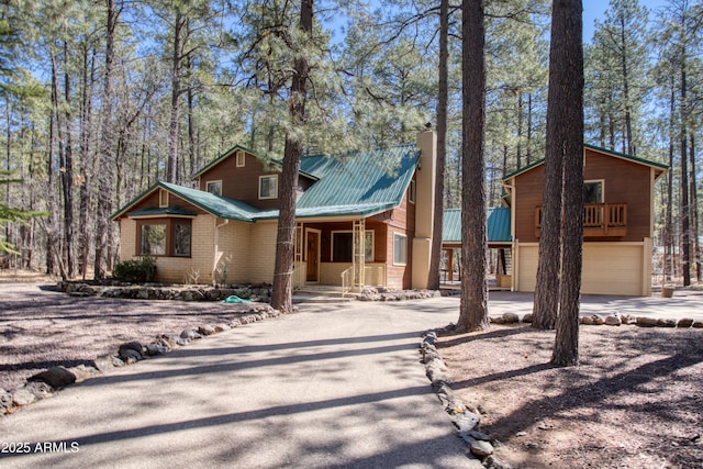 rustic home with a garage, a chimney, metal roof, and concrete driveway