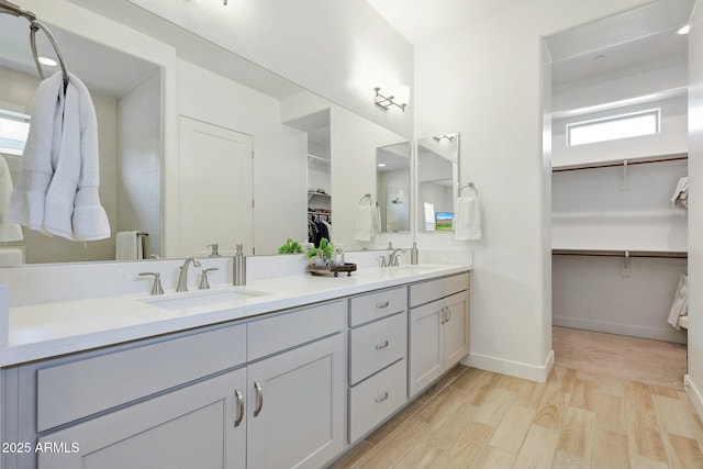bathroom with double vanity, wood finished floors, a sink, a walk in closet, and baseboards