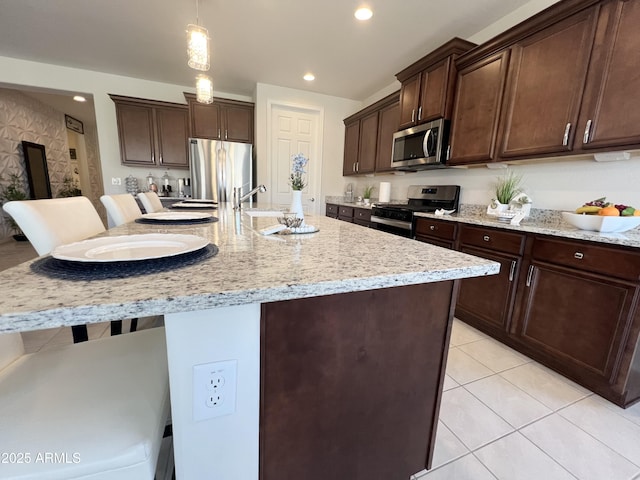 27636 W Runion Dr, Buckeye, AZ 85396 - kitchen featuring appliances with stainless steel finishes, dark brown cabinetry, a kitchen breakfast bar, decorative light fixtures, and a center island with sink