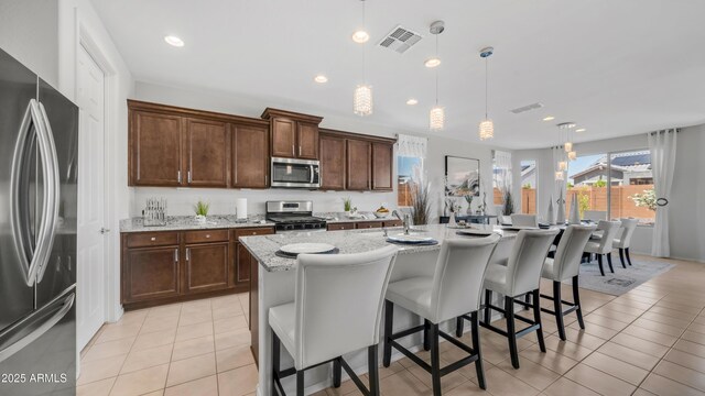 27636 W Runion Dr, Buckeye, AZ 85396 - kitchen with appliances with stainless steel finishes, light tile patterned floors, light stone counters, a breakfast bar area, and a center island with sink