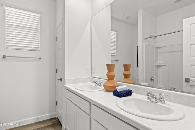 full bath featuring double vanity, baseboards, a sink, and wood finished floors