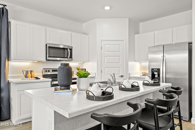 kitchen featuring stainless steel appliances, light countertops, white cabinets, and a center island with sink