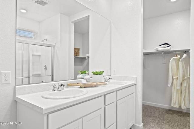 bathroom featuring visible vents, double vanity, a sink, and a walk in closet